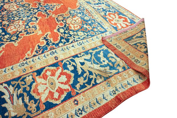 A rust red and navy patterned rug corner is folded over, showing the ornate main field and detailed border.