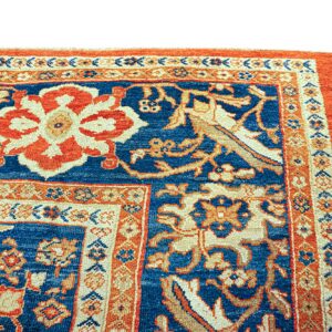 Detailed view of a traditional rug featuring a blue field with prominent orange and beige floral designs.
