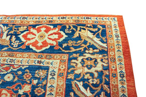 Detailed view of a traditional rug featuring a blue field with prominent orange and beige floral designs.