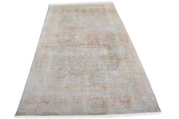 Pale gray rug with short fringe and a subtle, faded traditional pattern in rust and purple.