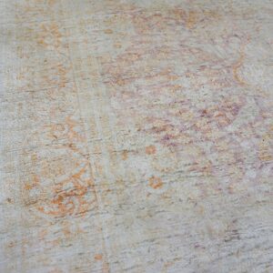 The textured surface of a rug shows faded traditional patterns in orange, purple, and cream.