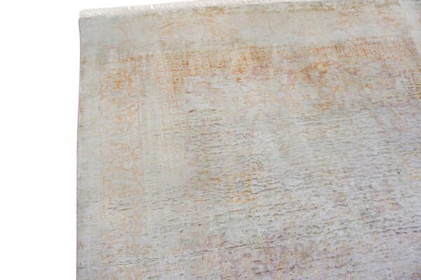 Distressed low pile rug close-up showing light grey, faded orange patterns, and short white fringe.