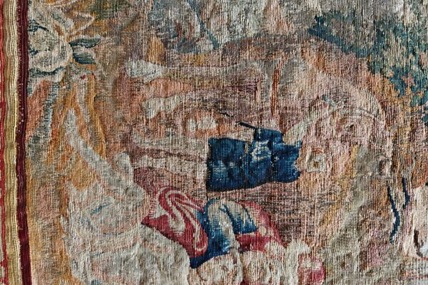 Aged, low-pile tapestry detail in muted tan, beige, red, and strong blue abstract patterns with a striped border.