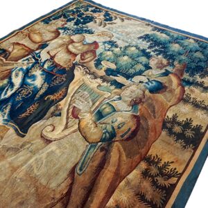 Detailed tapestry rug featuring robed figures and trees in rich blue, green, and faded gold colors.