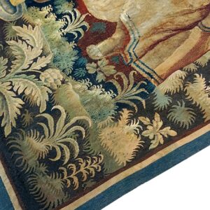 Detail of a low-pile rug with beige and green foliage, dark blue background, and a blue woven edge.