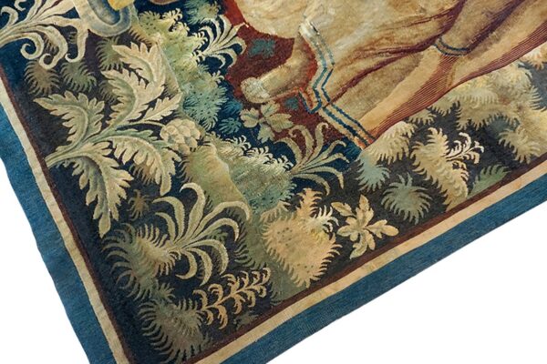 Detail of a low-pile rug with beige and green foliage, dark blue background, and a blue woven edge.
