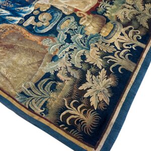 Corner detail of a dark blue tapestry rug featuring elaborate gold and light blue botanical scrollwork.
