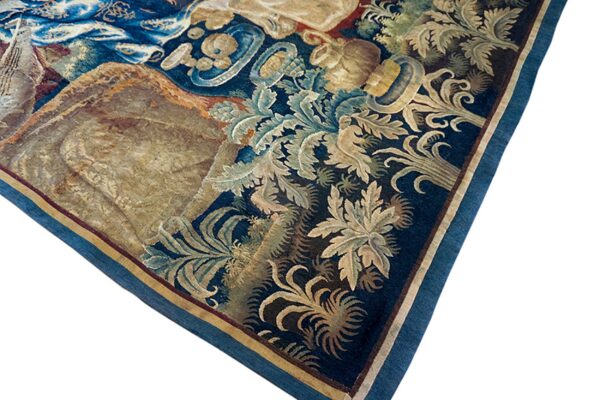 Corner detail of a dark blue tapestry rug featuring elaborate gold and light blue botanical scrollwork.