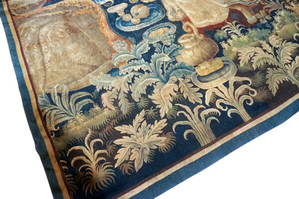 Worn flatweave rug section with a detailed blue, beige, and green acanthus leaf pattern and striped border.