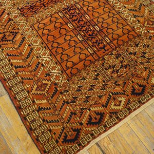 Highly patterned orange and dark blue area rug with detailed borders placed diagonally on natural wood planks.