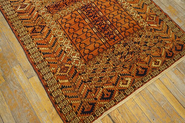 Highly patterned orange and dark blue area rug with detailed borders placed diagonally on natural wood planks.