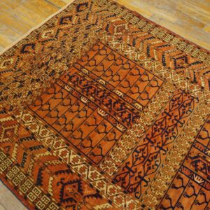 Geometric rug in deep orange, dark blue, and cream colors lies on a worn, light wood floor.