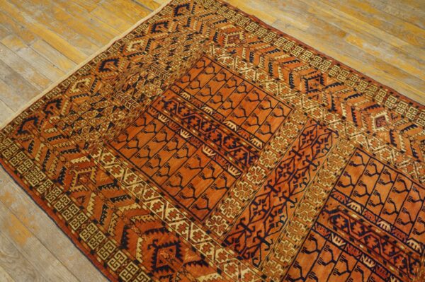 Geometric rug in deep orange, dark blue, and cream colors lies on a worn, light wood floor.