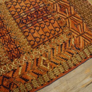 High-pile orange rug with contrasting dark blue geometric tribal designs on light wood planks.