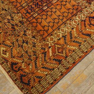 Close-up of an orange and dark blue tribal pattern rug on distressed light wood floors.