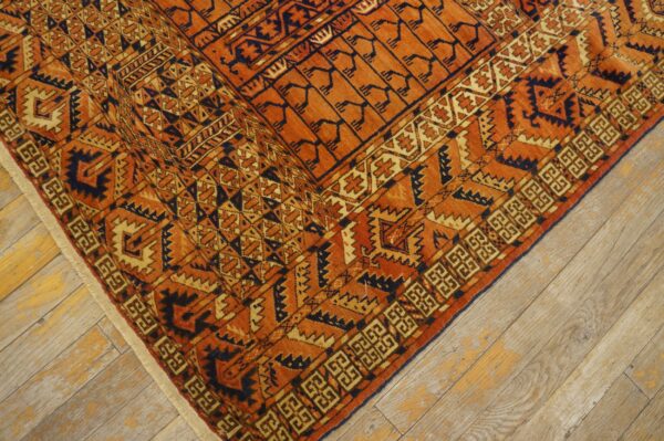 Close-up of an orange and dark blue tribal pattern rug on distressed light wood floors.