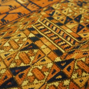 Detailed close-up of short-pile rug texture with complex geometric designs in orange, golden yellow, and navy.