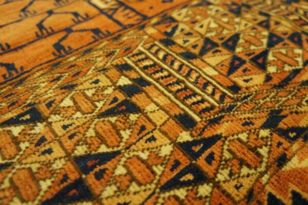 Detailed close-up of short-pile rug texture with complex geometric designs in orange, golden yellow, and navy.