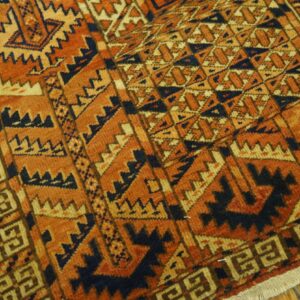 Close-up of a high-pile rug with geometric patterns in rust orange, navy, and tan on a wood floor.