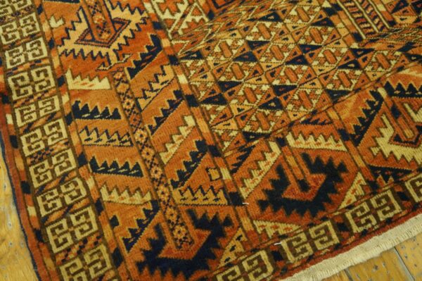 Close-up of a high-pile rug with geometric patterns in rust orange, navy, and tan on a wood floor.