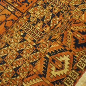 A tightly patterned rug in rust, gold, and navy blue, curving over light wooden floorboards.