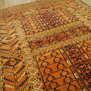 Low pile rug featuring burnt orange, navy, and tan geometric motifs rests on light wood plank flooring.