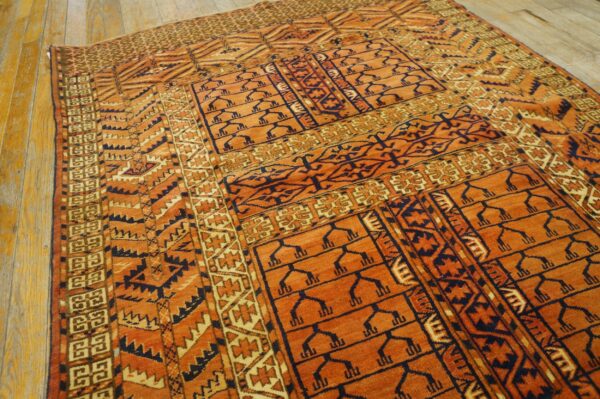 Low pile rug featuring burnt orange, navy, and tan geometric motifs rests on light wood plank flooring.