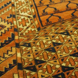 Close-up of a medium pile rug showing geometric designs in orange, gold, and dark blue colors.