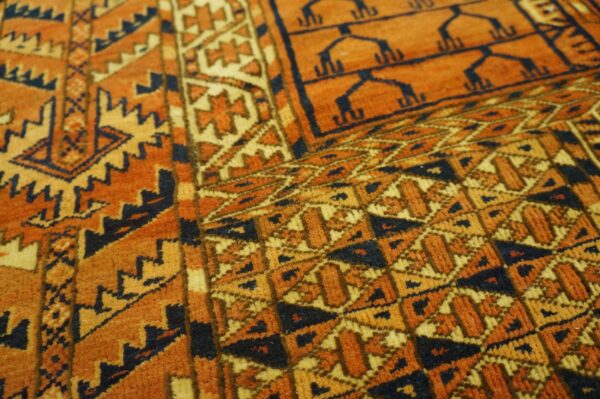 Close-up of a medium pile rug showing geometric designs in orange, gold, and dark blue colors.