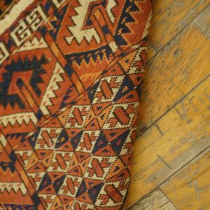 Geometric low-pile rug featuring orange, navy, and cream colors on distressed yellow wood flooring.