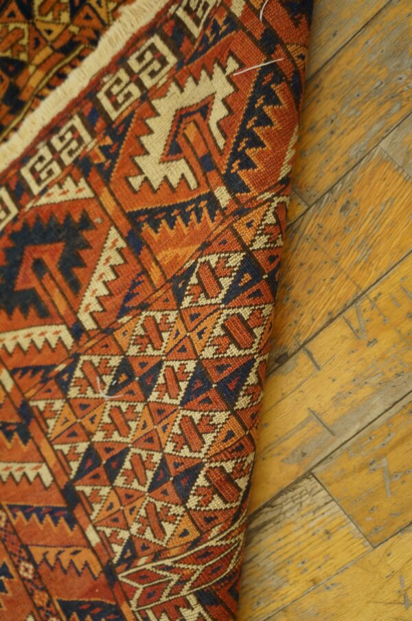 Geometric low-pile rug featuring orange, navy, and cream colors on distressed yellow wood flooring.