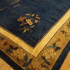A deep blue floral rug corner features gold and olive borders, resting on rustic hardwood flooring.