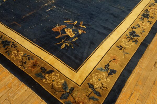 A deep blue floral rug corner features gold and olive borders, resting on rustic hardwood flooring.