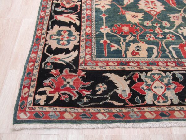 Traditional rug corner featuring teal, black, red, and beige floral patterns on pale wood flooring.