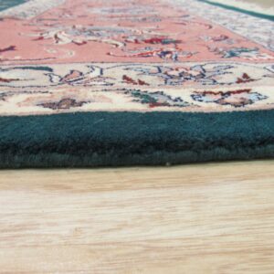 Close-up shows a thick teal rug border and pink floral pattern resting on light wooden floors.