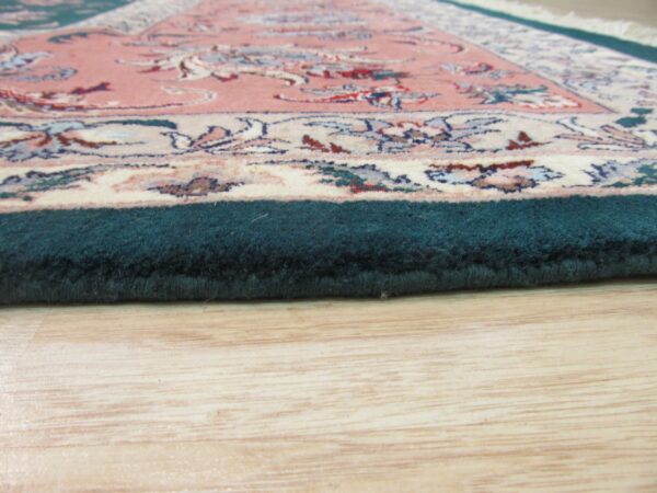 Close-up shows a thick teal rug border and pink floral pattern resting on light wooden floors.