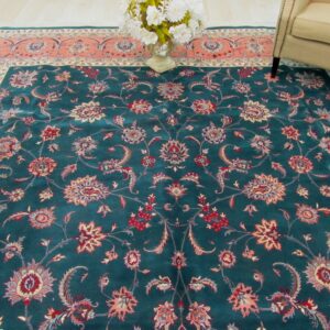 Traditional teal rug featuring red and coral floral motifs, partially visible under a neutral armchair.