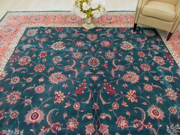 Traditional teal rug featuring red and coral floral motifs, partially visible under a neutral armchair.