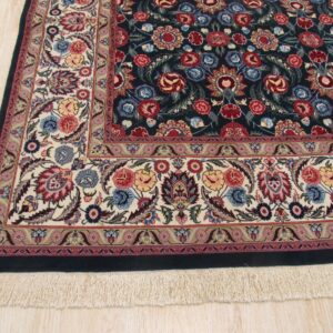 Dark blue floral rug with multi-colored motifs and wide ivory border rests on light wood floor.