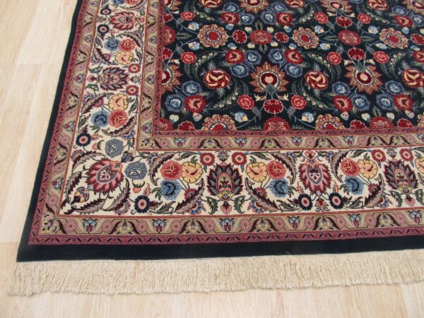 Dark blue floral rug with multi-colored motifs and wide ivory border rests on light wood floor.