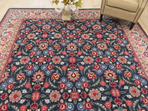 Plush dark blue rug with a dense red and multicolor floral pattern next to an upholstered armchair.