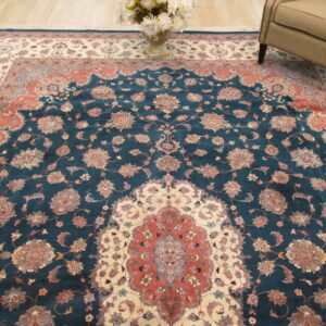 Traditional teal rug with terracotta and ivory floral medallion sits beneath an armchair and flower vase.