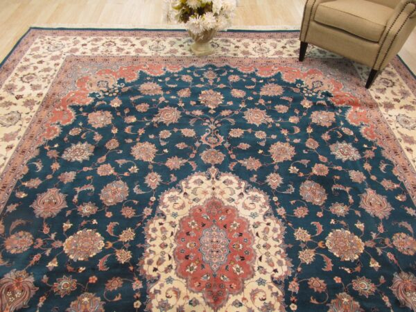 Traditional teal rug with terracotta and ivory floral medallion sits beneath an armchair and flower vase.