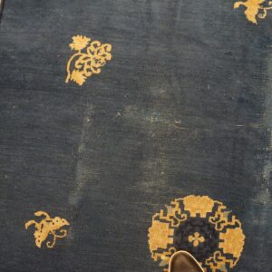 Detail of blue rug showing gold floral medallions, geometric borders, and visible low pile wear.