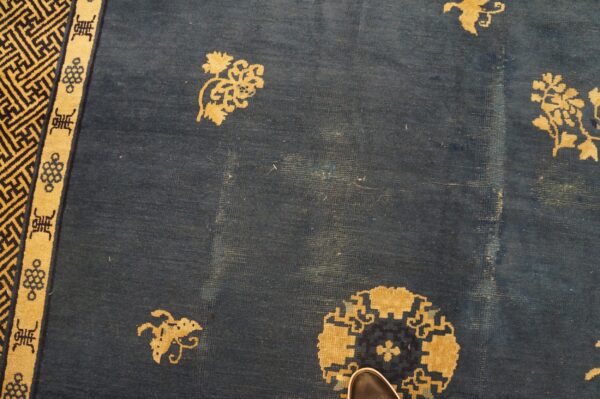 Detail of blue rug showing gold floral medallions, geometric borders, and visible low pile wear.