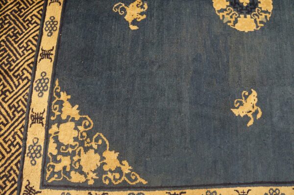 Deep indigo rug with a dense gold geometric border and scrolling floral corner designs.