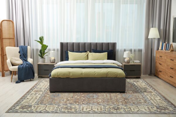 A muted traditional brown and beige rug defines a modern bedroom with light flooring and grey furniture.