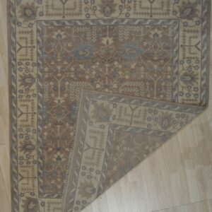 Brown and tan patterned rug with blue accents displayed on light wood flooring with a corner folded over.