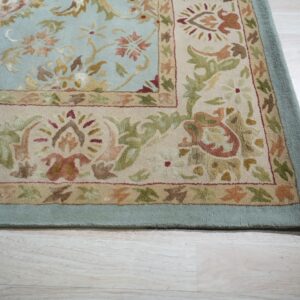 Pale blue rug with a beige and floral border lies on light blonde wood flooring.