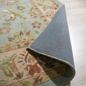 Light blue floral rug with a beige border rolled back showing gray backing on light wood floor.